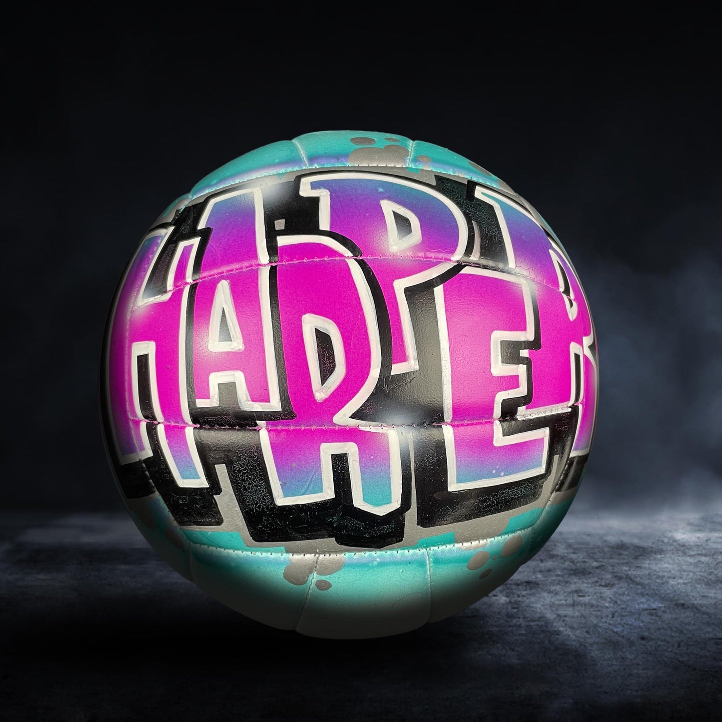 A colorful sports ball with the word "HAPPY" painted on it in a stylized, graffiti-like design.