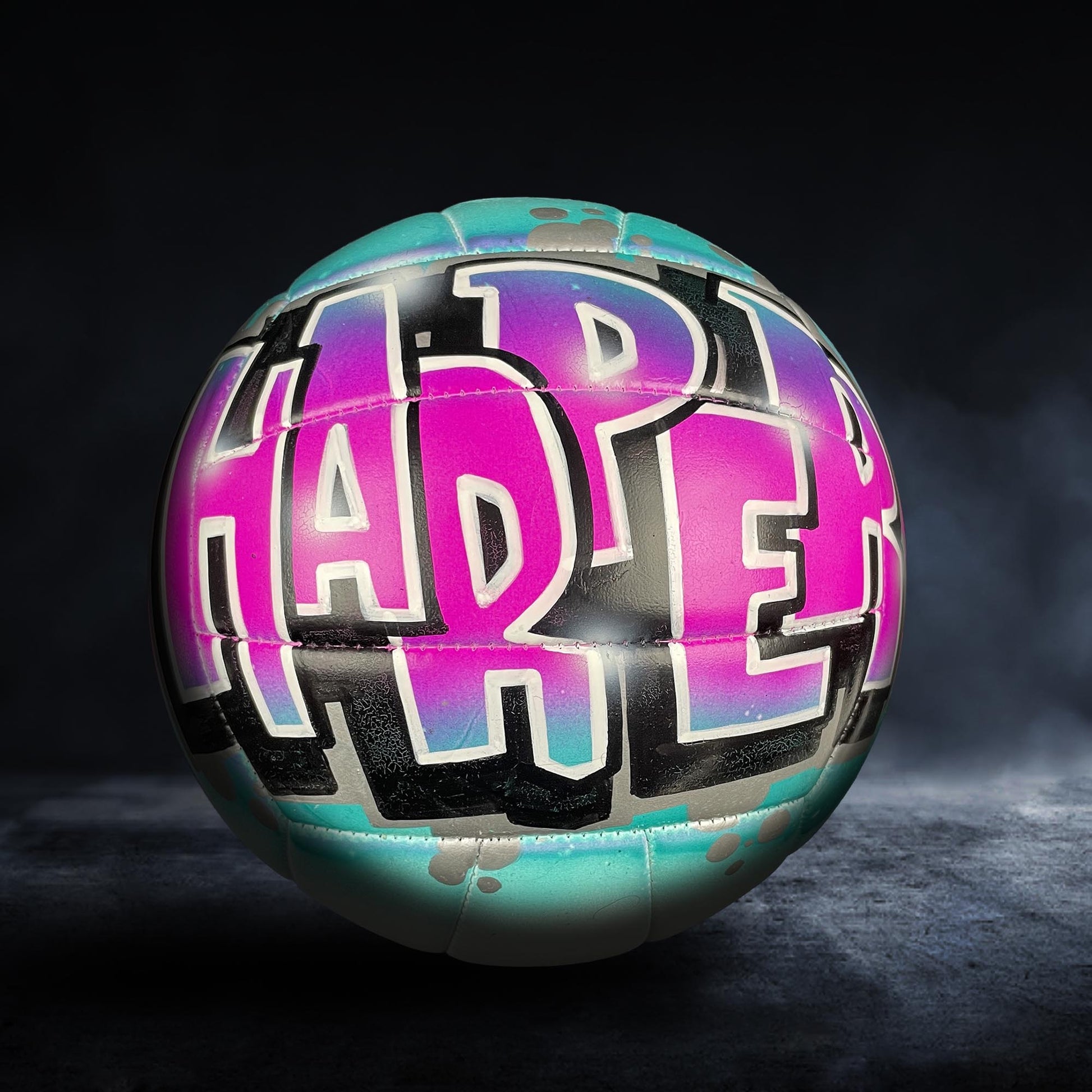 A colorful sports ball with the word "HAPPY" painted on it in a stylized, graffiti-like design.