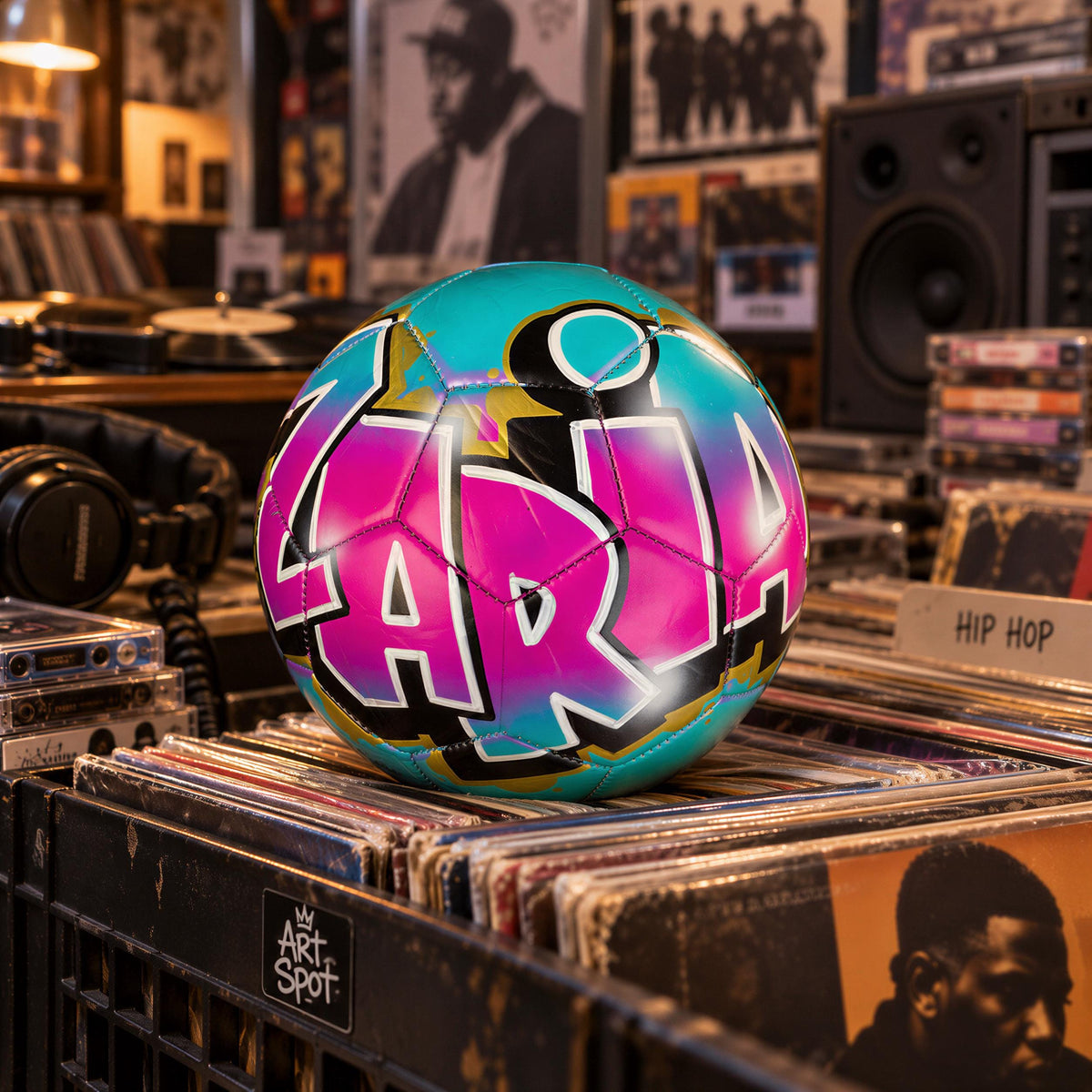 A colorful soccer ball with the name "LARIA" painted on it, surrounded by various items such as records and headphones, in what appears to be a music or record store setting.