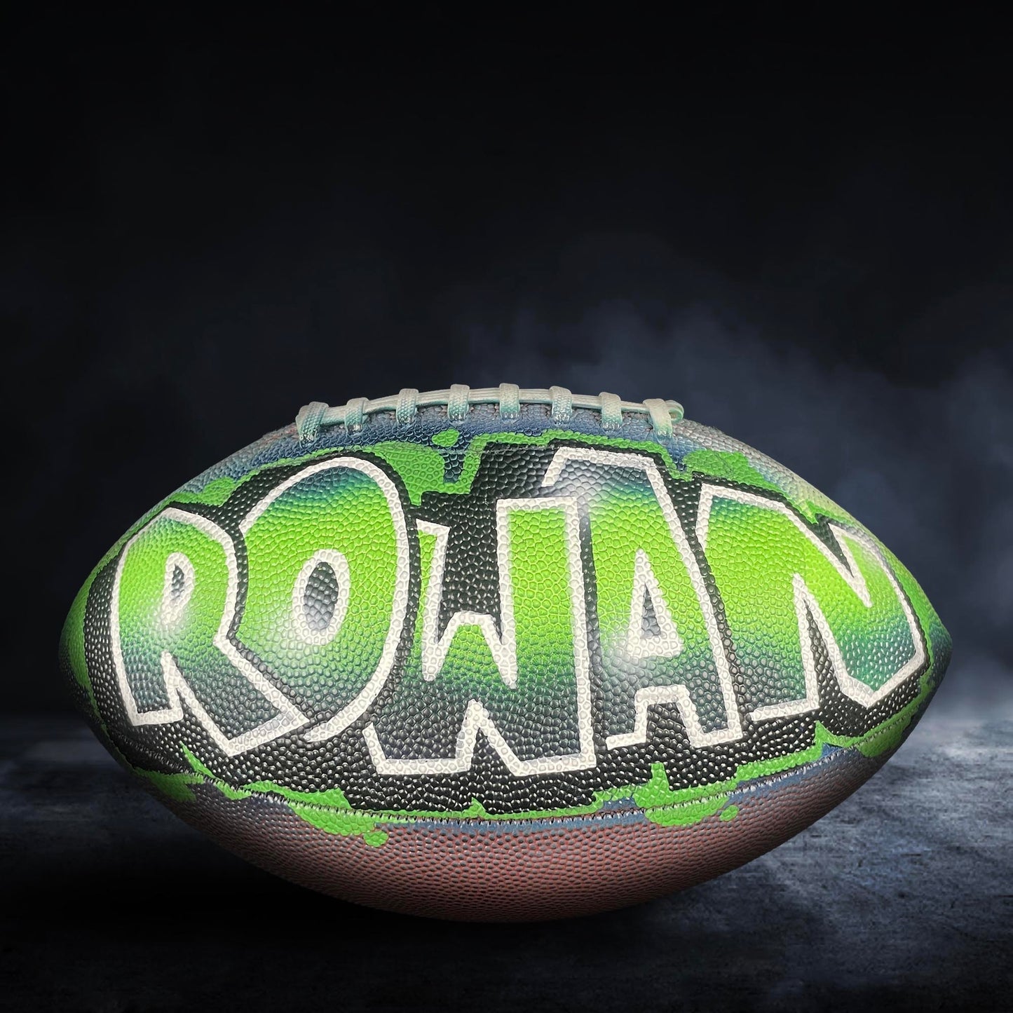 A football with the word "Rowan" painted on it, set against a dark background with smoke or fog.