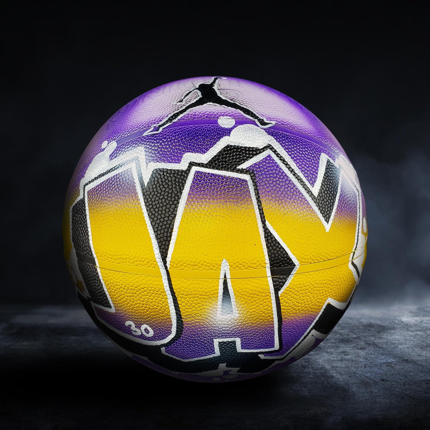 A basketball with the word "JAY" painted on it, featuring a purple and yellow color scheme.