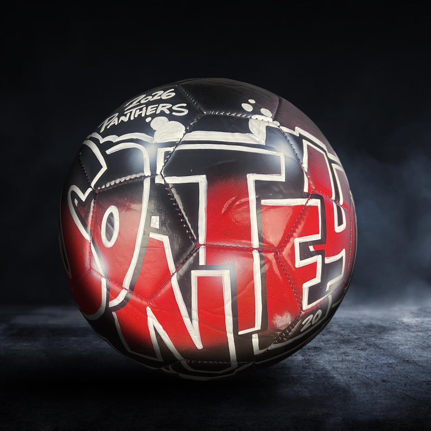 A soccer ball with the word "VANILLA" painted on it, featuring a mix of red and black colors.