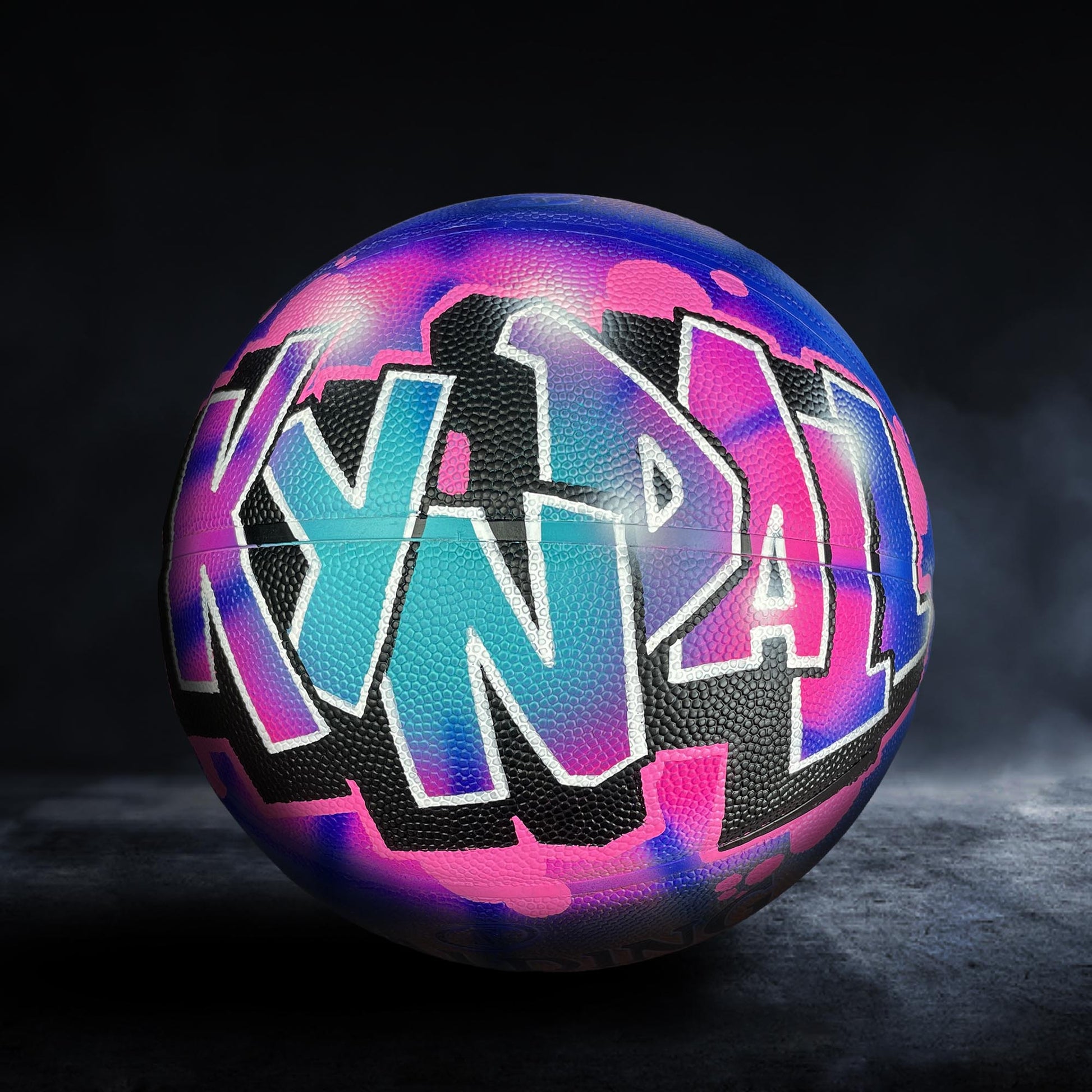 A colorful basketball with graffiti-style lettering on it, set against a dark background.