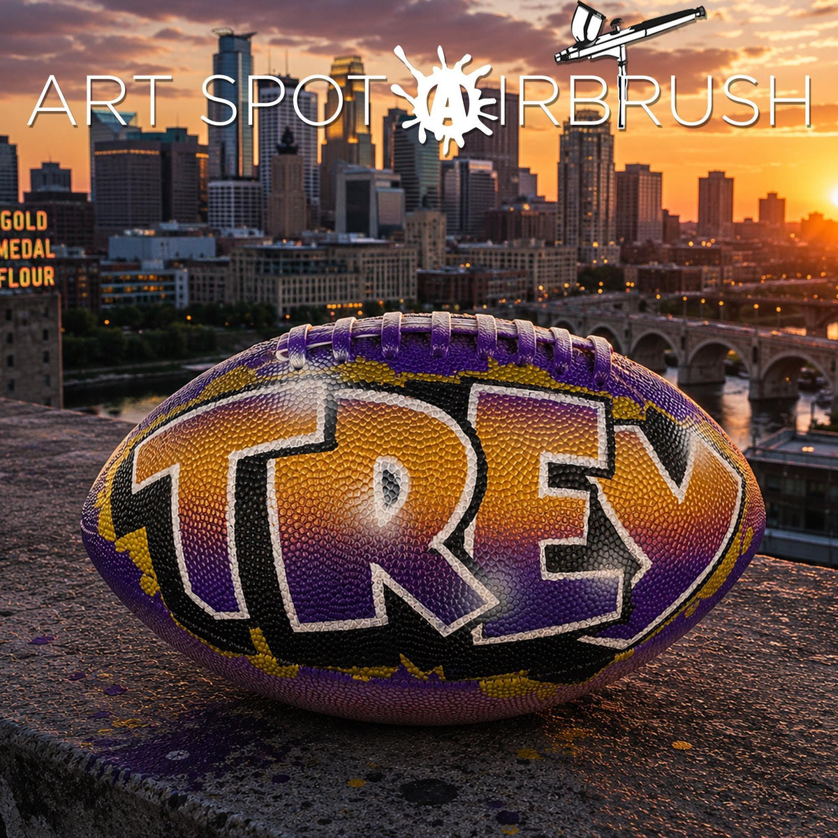 A custom football personalized with the name "TREY" painted on it, set against the backdrop of a city skyline at sunset.