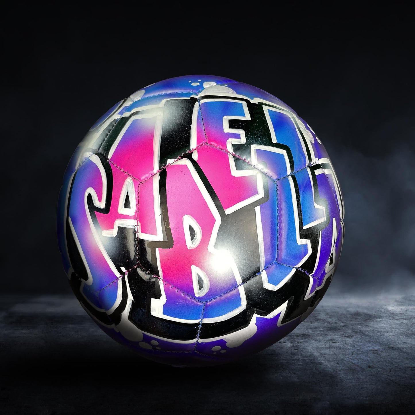 A colorful soccer ball with graffiti-style lettering on it, set against a dark background.