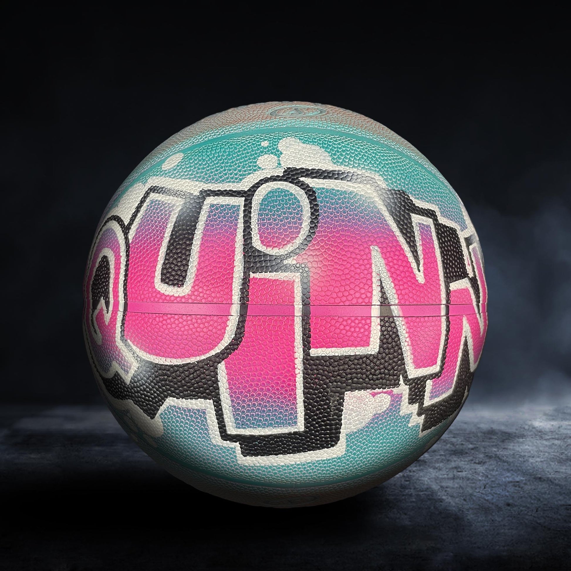 A colorful basketball with the word "QUINX" painted on it, featuring a mix of pink, blue, and black colors.