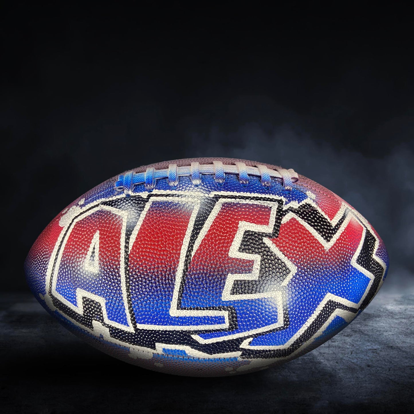 A football with the name "ALEX" painted on it, featuring a colorful design with red, blue, and white colors.