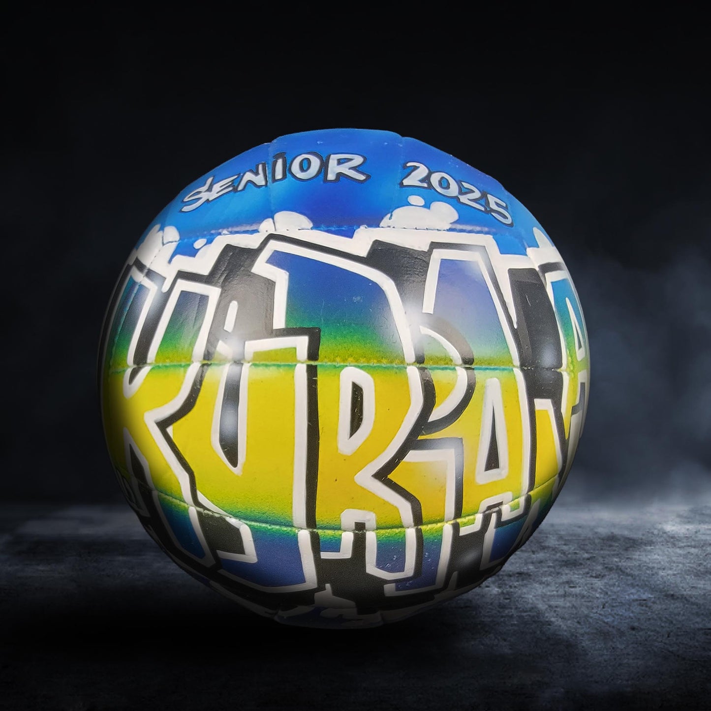 A colorful sports ball with the word "SENIOR" and "2025" printed on it, against a dark background.