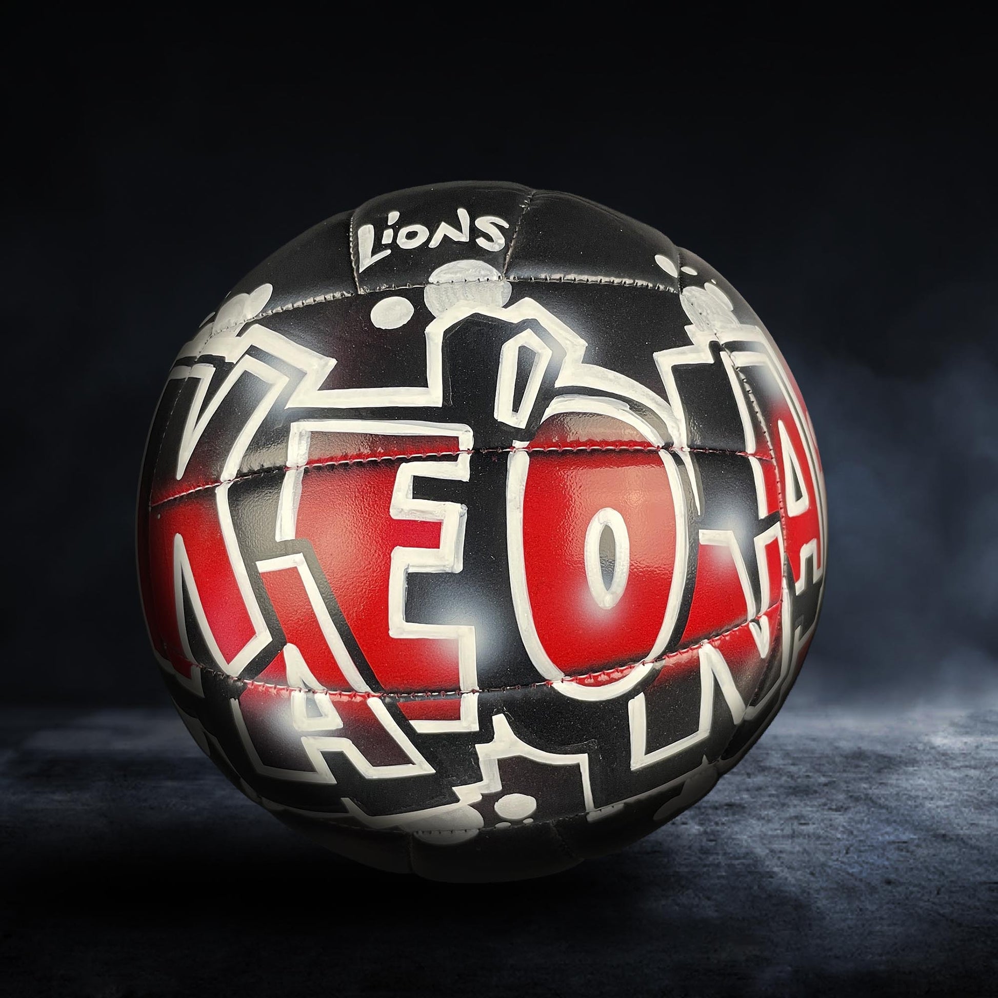 A black and red soccer ball with the word "LIONS" written on it, against a dark background.