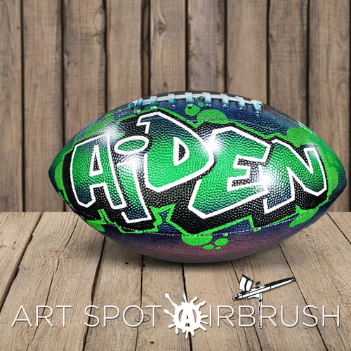 A personalized football with the name "Aiden" painted on it, sitting on a wooden surface.