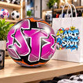 A colorful soccer ball with graffiti-style designs is displayed on a table next to a white shopping bag with a graffiti-style design.