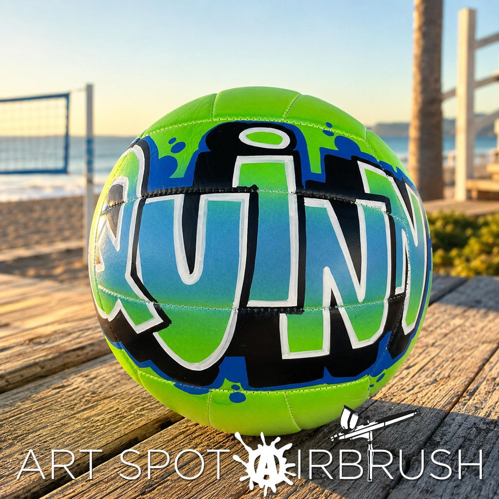 A neon green and blue custom volleyball personalized with the word "QUINN" painted on it, sitting on a wooden surface.