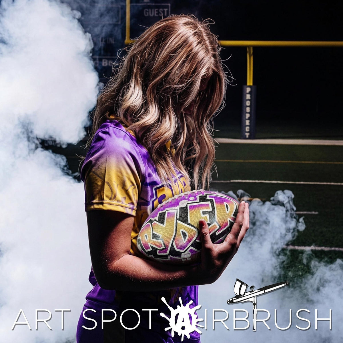 A woman in a purple and yellow uniform holding a custom football, personalized with the name Ryder, standing on a field with smoke in the background.