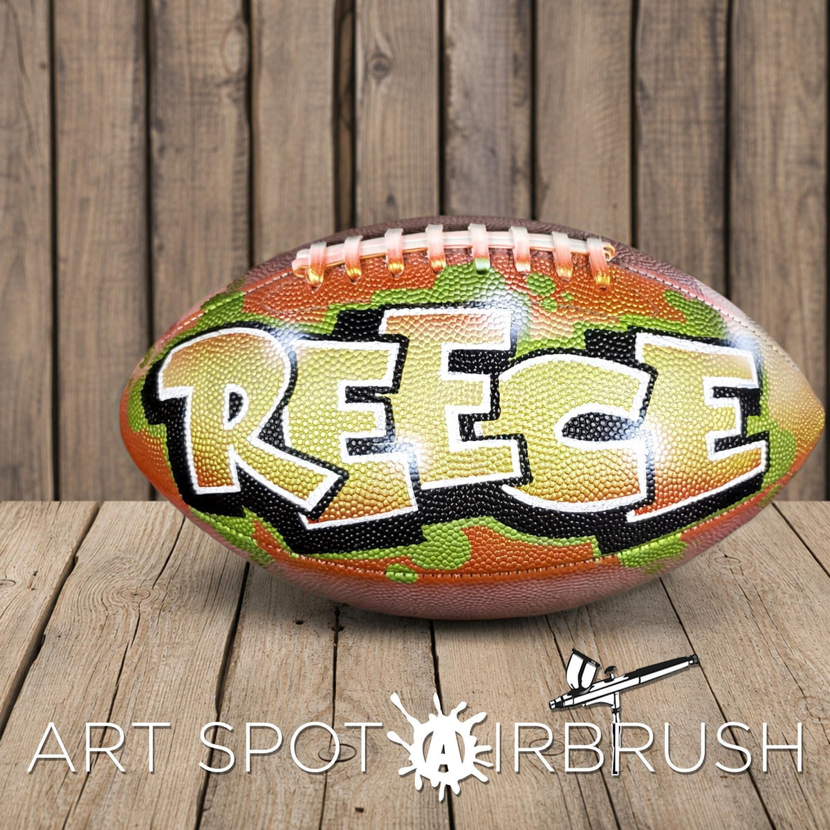 A football with the name "REECE" painted on it, sitting on a wooden surface.