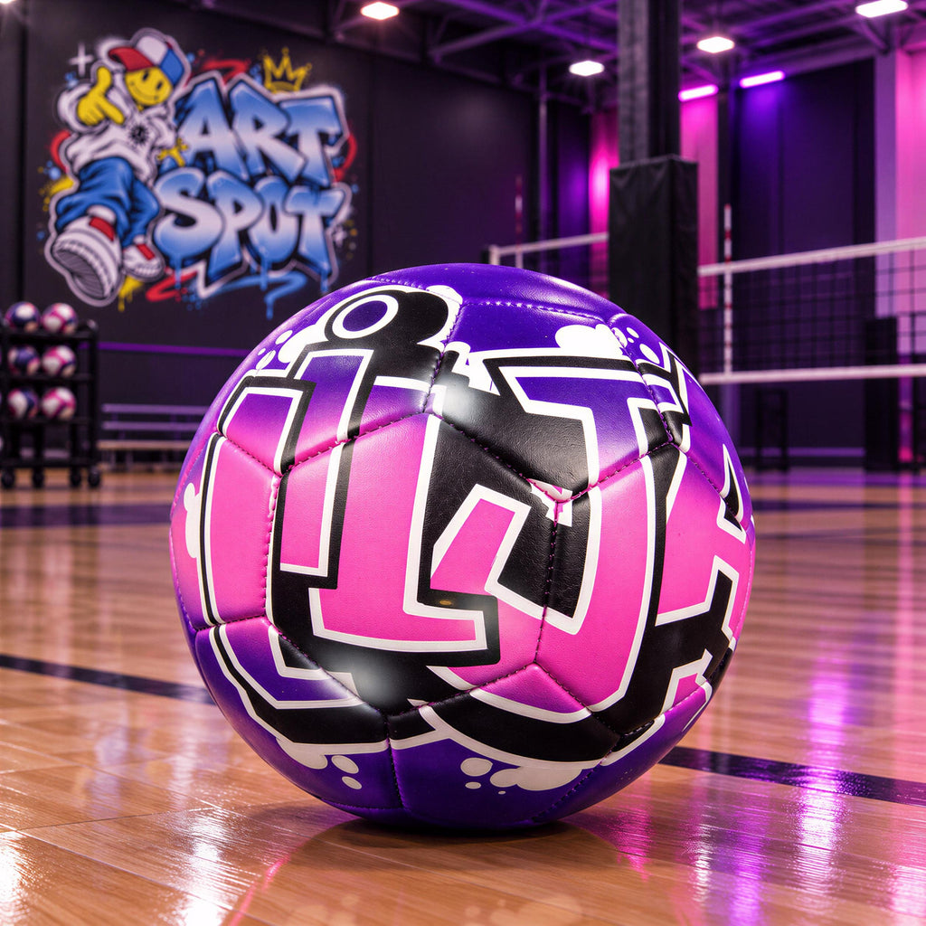 A purple and black soccer ball with graffiti-style lettering is displayed on a wooden floor in a brightly lit indoor sports facility.