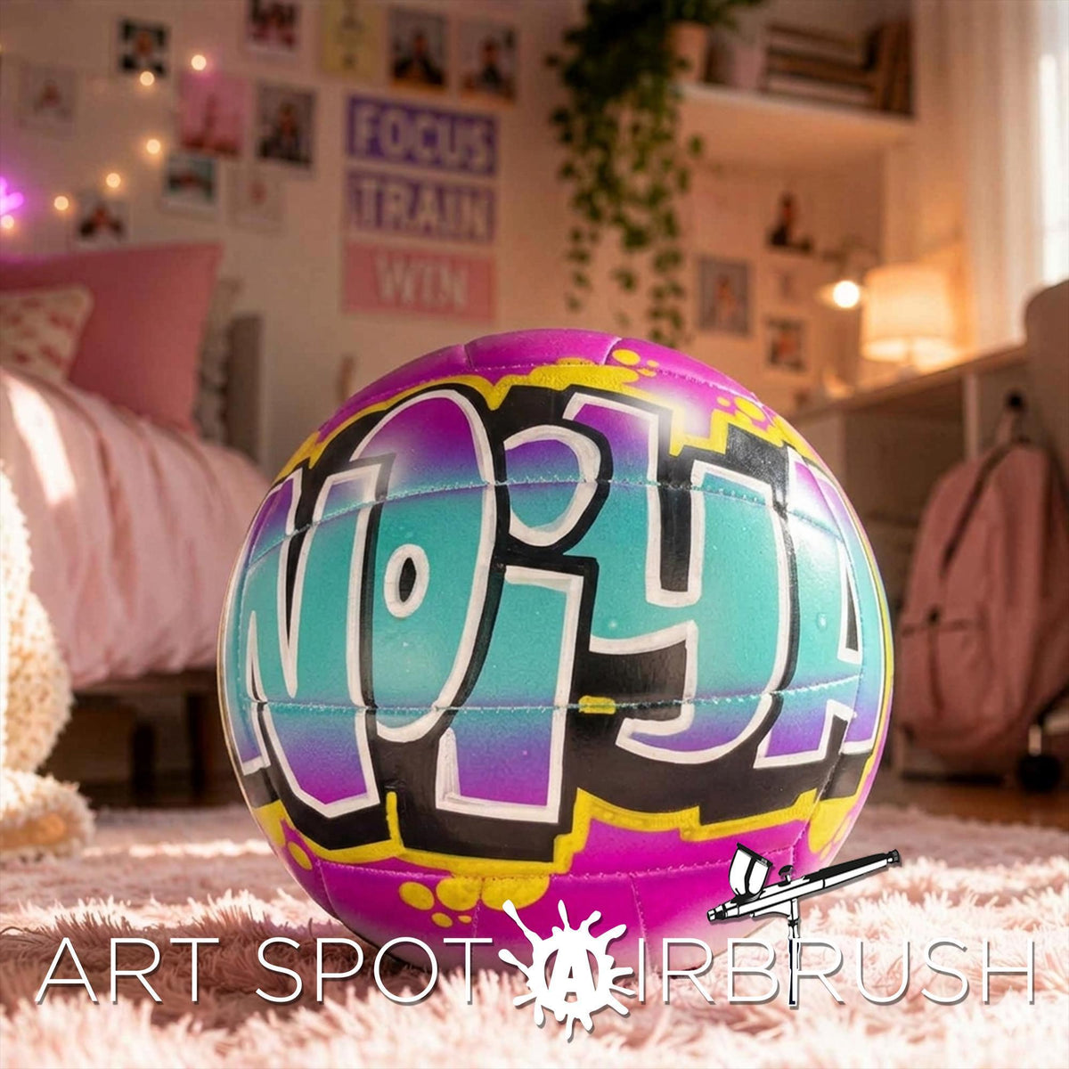 A colorful, graffiti-style personalized custom volleyball with the word "NOIYA" painted on it, sitting on a pink carpet in a bedroom with various decorations and furniture.
