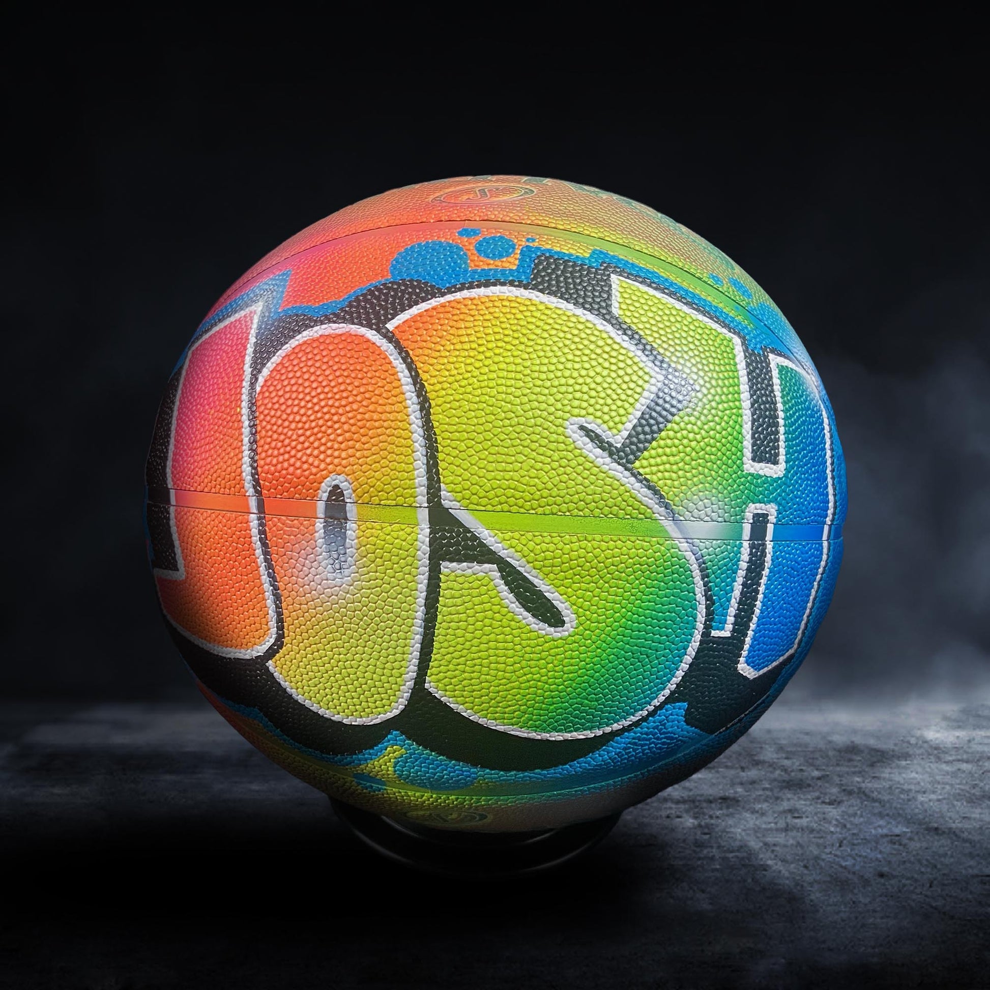 A colorful basketball with the name "Josh" painted on it, sitting on a dark surface.
