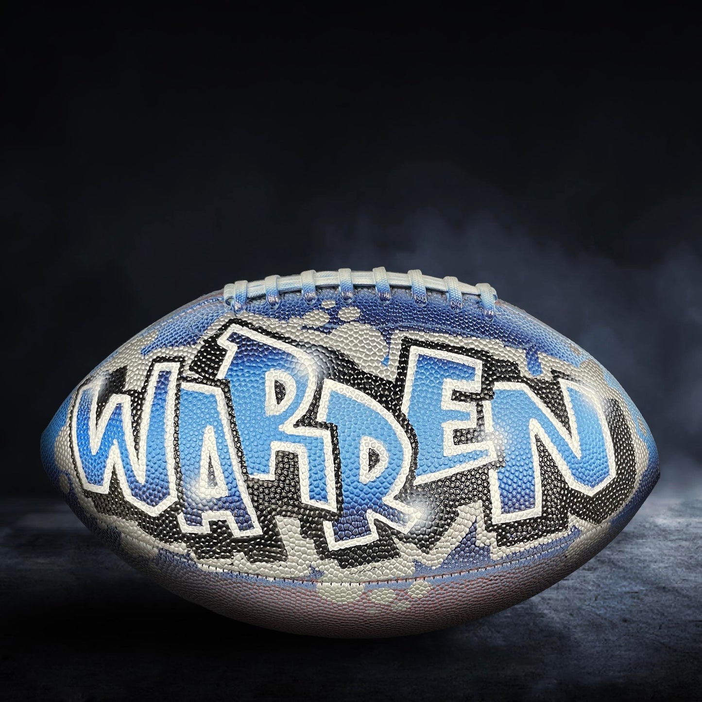 A football with the name "WARREN" painted on it, against a dark background with smoke or fog.