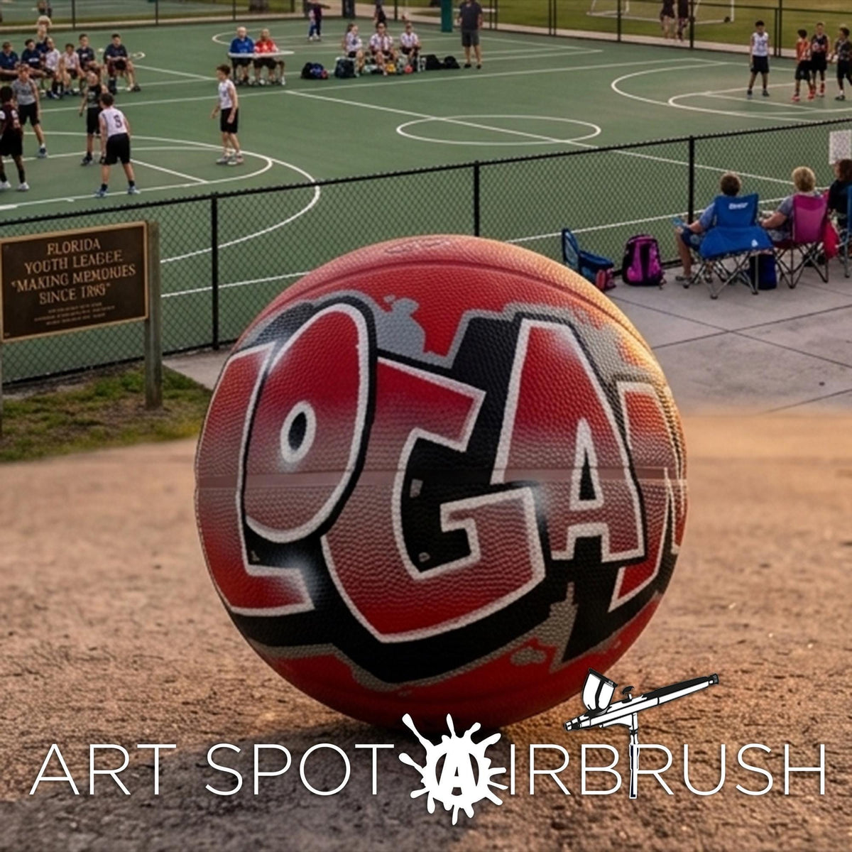 A red basketball with the word "LOGAN" painted on it, sitting on a dirt surface in a park. There are people playing basketball in the background, and a sign for Florida Youth Leagues is visible.