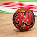 A red basketball with graffiti text on it, sitting on a wooden floor.