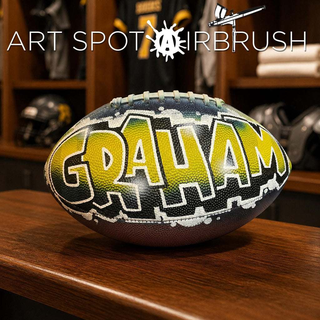 A custom football personalized with the name "GRAHAM" painted on it, sitting on a wooden surface.