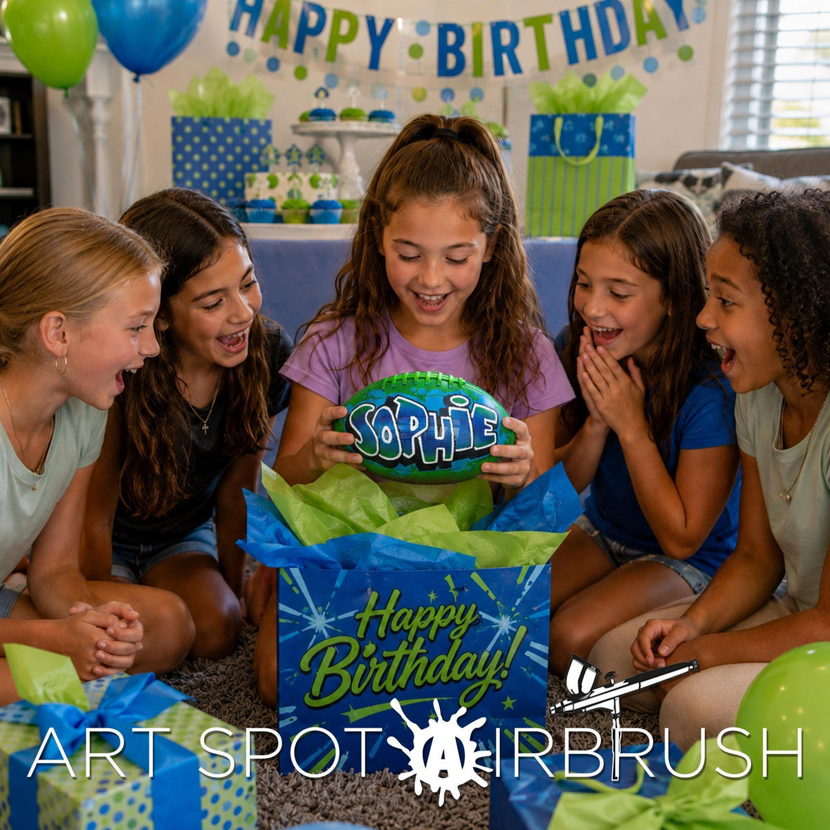 A group of young girls gathered around a birthday girl, who is holding a green custom football personalized with the name "Sophie" written on it. The girls are smiling and appear to be celebrating the birthday together.