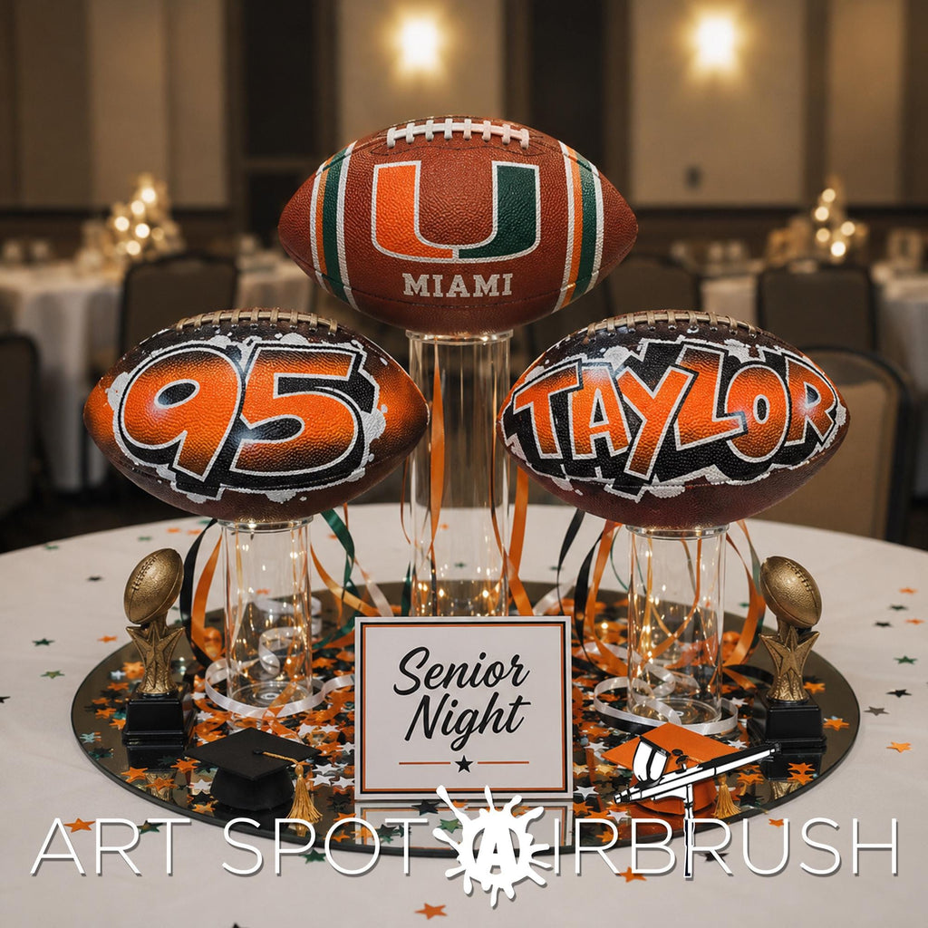 a table with three custom footballs personalized ,with the letters "95" , the Miami U, and " Taylor" and are placed on a tablecloth with confetti. There is also a sign that reads " Senior Night" in the foreground.