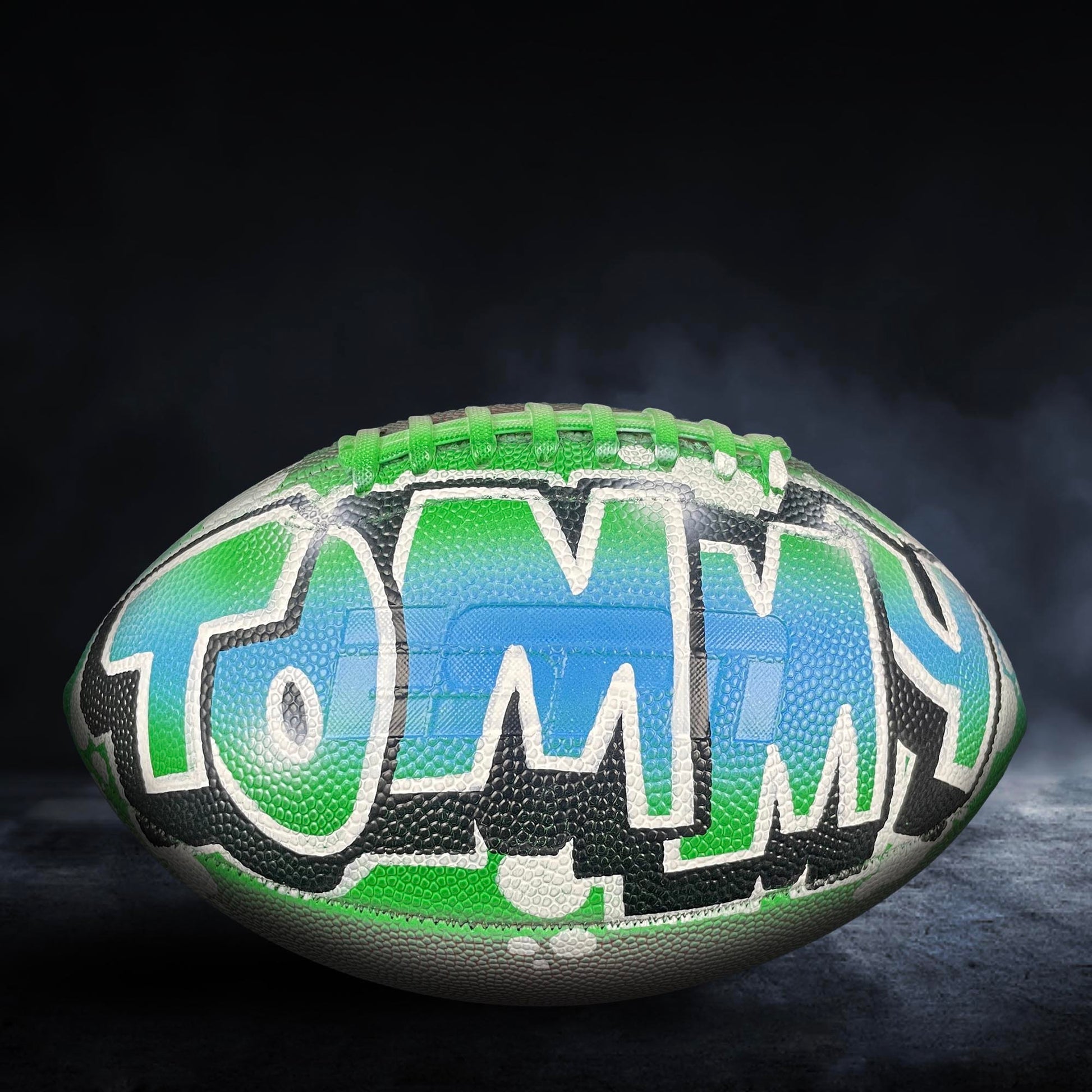 A football with the name "TOMMY" painted on it, featuring a colorful and stylized design.