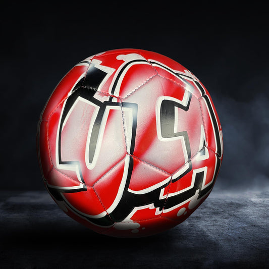 A red and black soccer ball with a stylized design on it, placed on a dark surface.