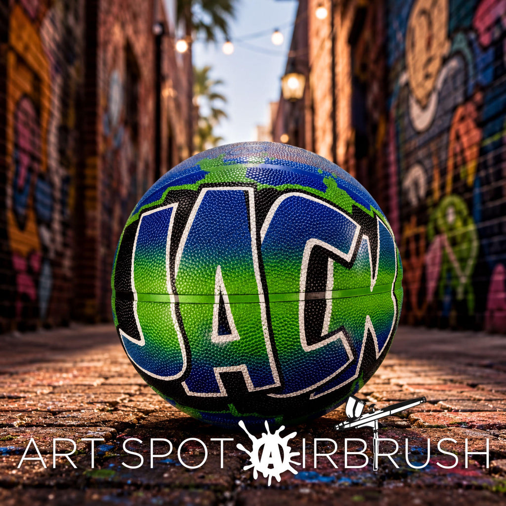 A colorful basketball with the word "JACK" painted on it, sitting on a brick surface in an urban setting with graffiti-covered walls in the background.