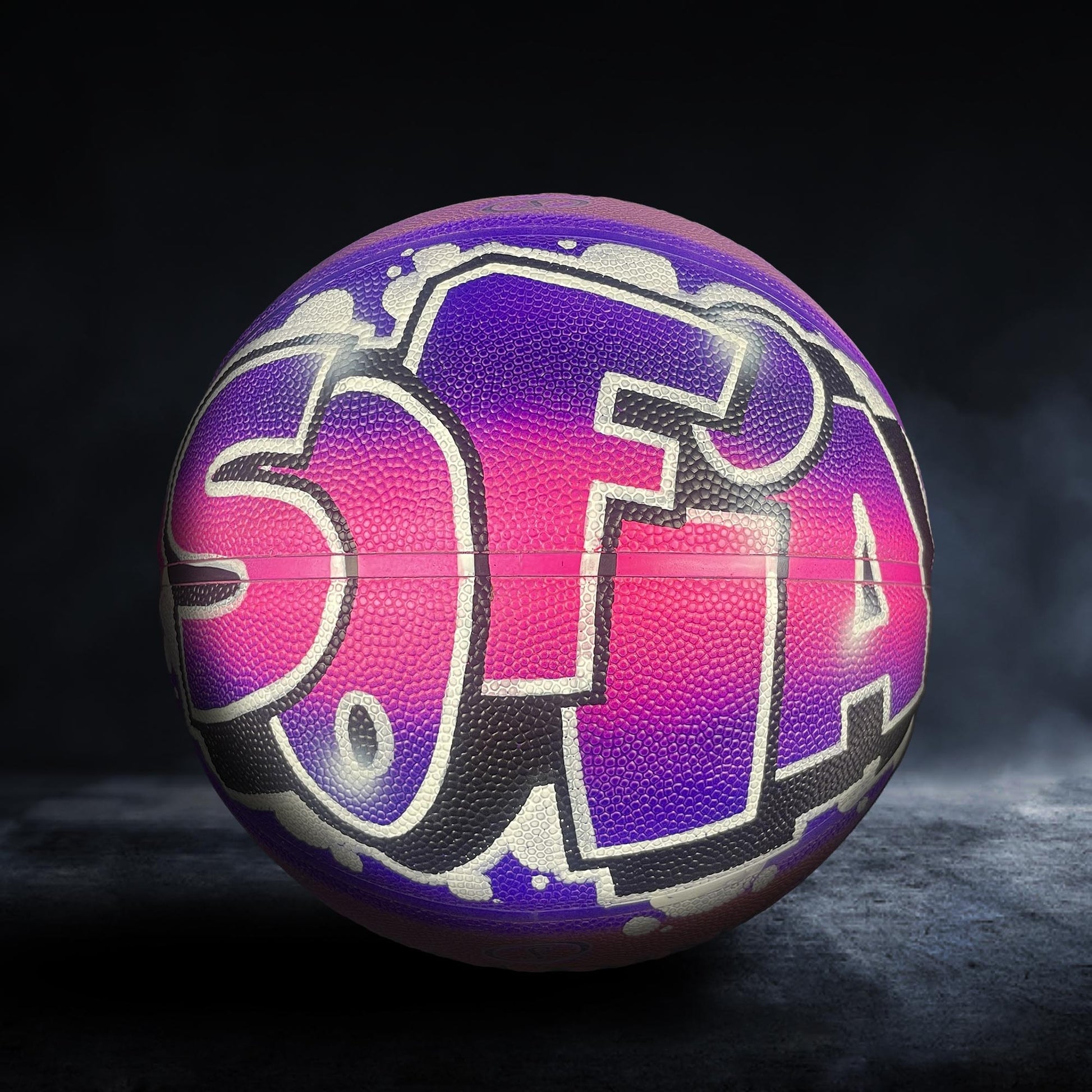 A colorful basketball with graffiti-style text on it, set against a dark background.