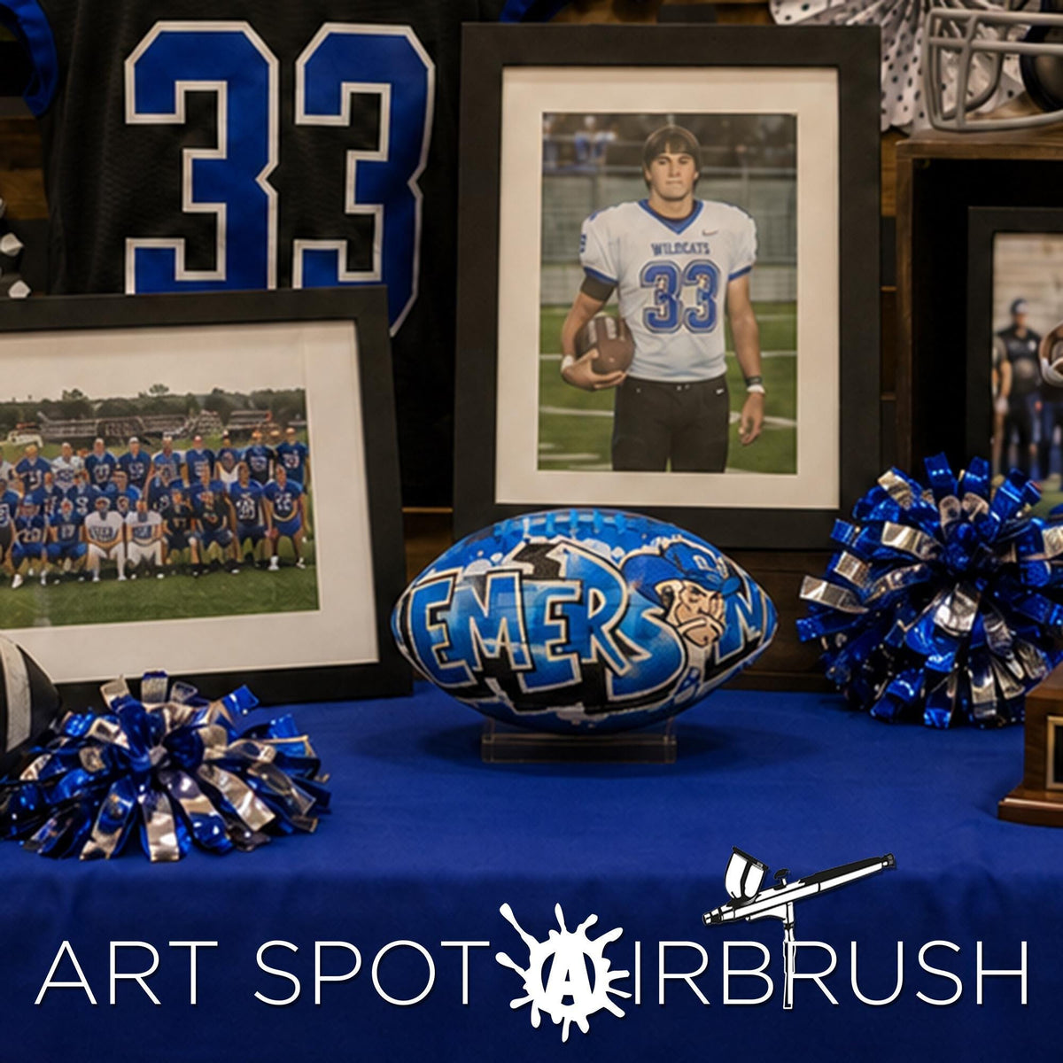 a display of sports memorabilia, including framed photos of a football team, a custom football personalized with a name and character, and a framed jersey with the number 33. The display is set against a blue background, and there is text at the bottom that reads "ART SPOT AIRBRUSH".